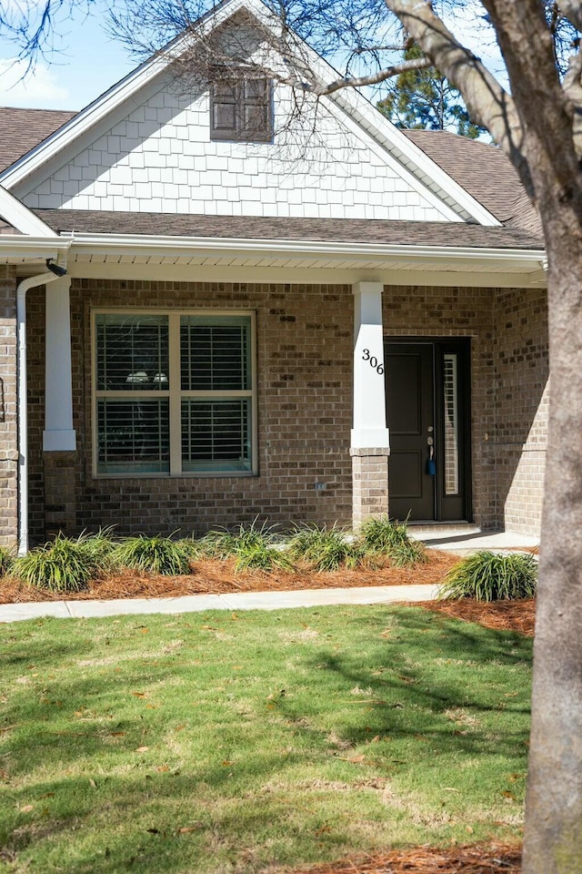 view of front of home with brick siding, a shingled roof, and a front lawn