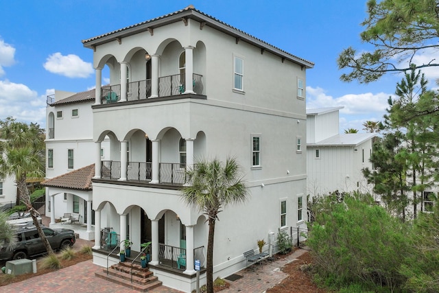 rear view of house featuring stucco siding, a tile roof, and a balcony