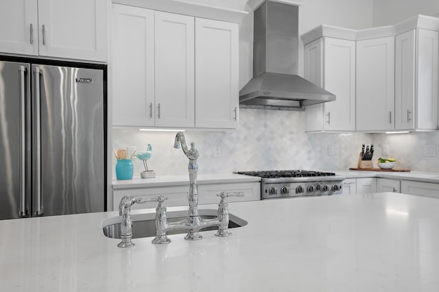 kitchen with backsplash, white cabinetry, high quality fridge, and wall chimney exhaust hood