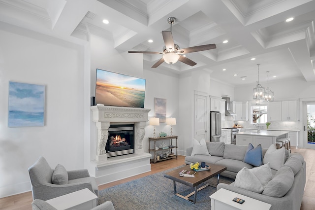 living room featuring light wood finished floors, coffered ceiling, a premium fireplace, beamed ceiling, and ceiling fan with notable chandelier