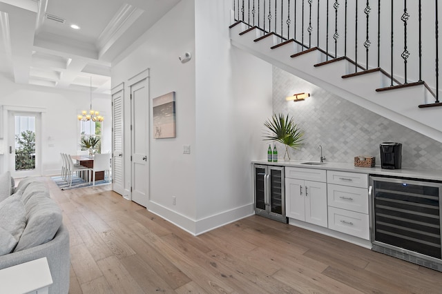 bar featuring indoor wet bar, light wood finished floors, beverage cooler, and coffered ceiling