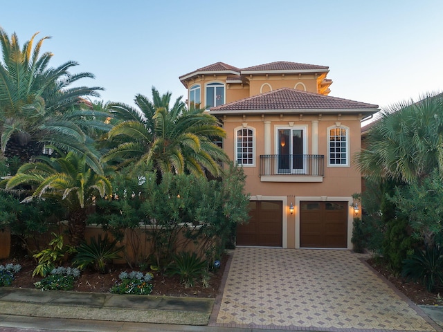 mediterranean / spanish-style home with a balcony, an attached garage, stucco siding, a tile roof, and decorative driveway