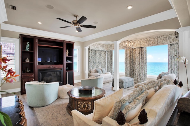 living area with decorative columns, wood finished floors, visible vents, and ceiling fan