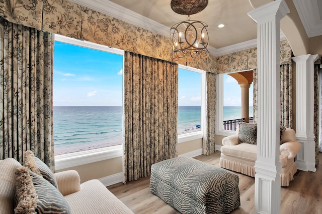 interior space featuring wood finished floors, a water view, ornate columns, and ornamental molding