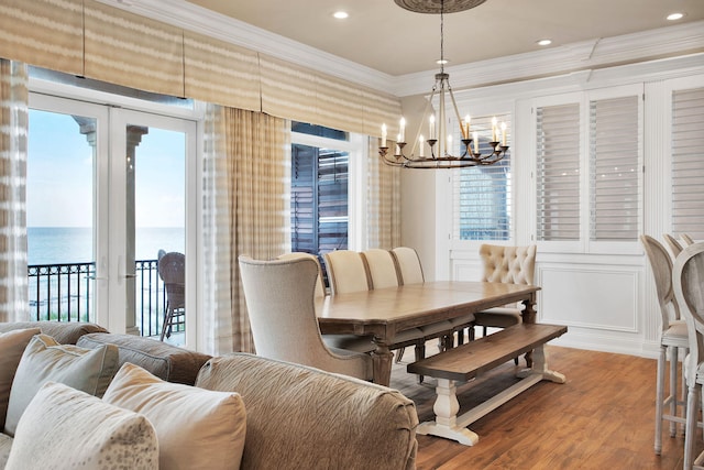 dining space with a water view, a chandelier, ornamental molding, wood finished floors, and a decorative wall