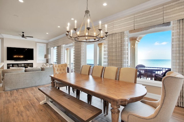 dining space with a water view, ornamental molding, ceiling fan with notable chandelier, wood finished floors, and recessed lighting