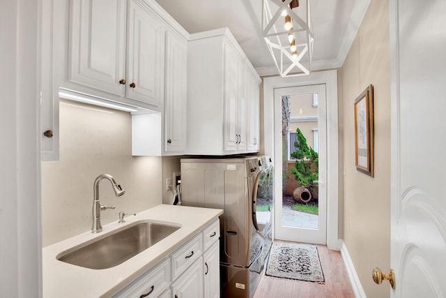 clothes washing area with baseboards, washer and clothes dryer, light wood-style flooring, cabinet space, and a sink