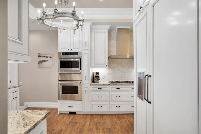 kitchen featuring a chandelier, light wood-style flooring, appliances with stainless steel finishes, white cabinetry, and wall chimney exhaust hood