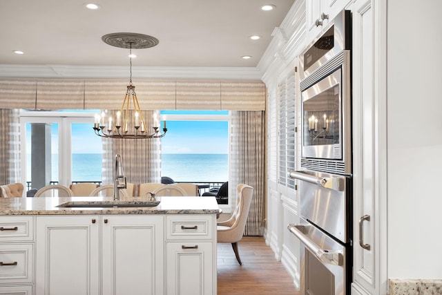 kitchen with crown molding, a water view, a chandelier, white cabinets, and a sink