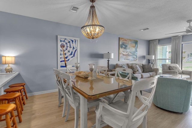 dining space featuring light wood-type flooring, visible vents, baseboards, and ceiling fan with notable chandelier