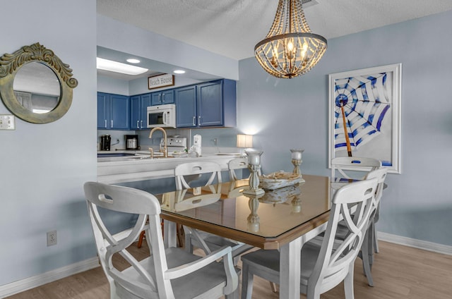 dining space with light wood-style flooring, baseboards, a chandelier, and a textured ceiling