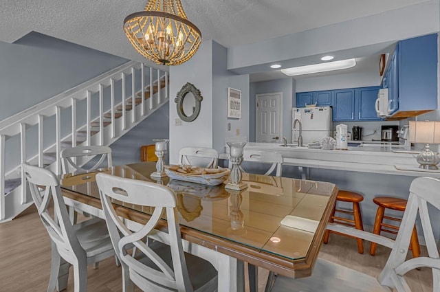 dining space featuring a chandelier, light wood-type flooring, a textured ceiling, and stairs