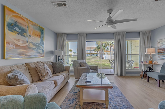 living area featuring visible vents, ceiling fan, a textured ceiling, and wood finished floors