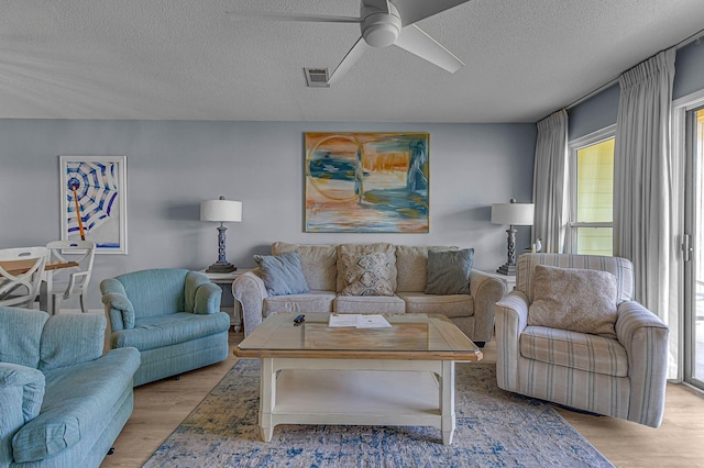 living area with ceiling fan, a textured ceiling, visible vents, and light wood-style floors