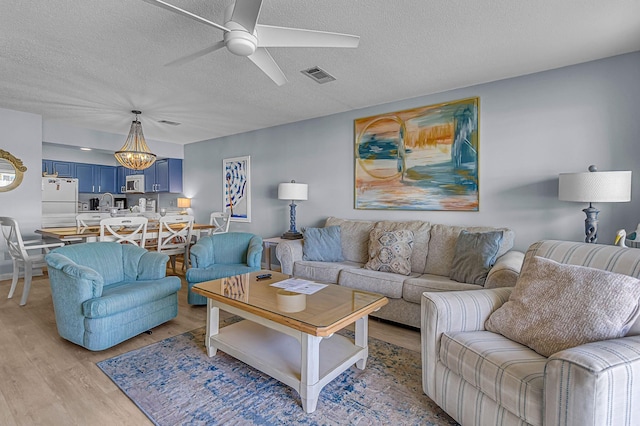 living room with light wood-type flooring, ceiling fan, visible vents, and a textured ceiling