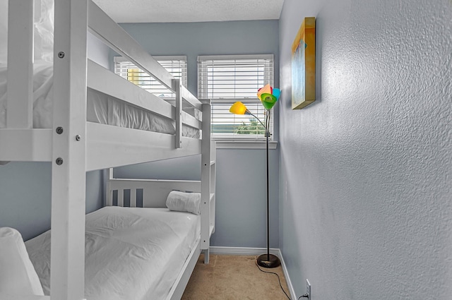 carpeted bedroom with a textured ceiling, a textured wall, and baseboards