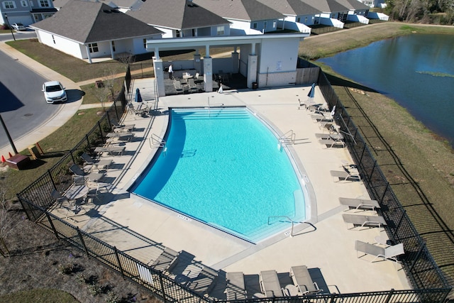 community pool featuring a patio, a water view, fence, and a residential view