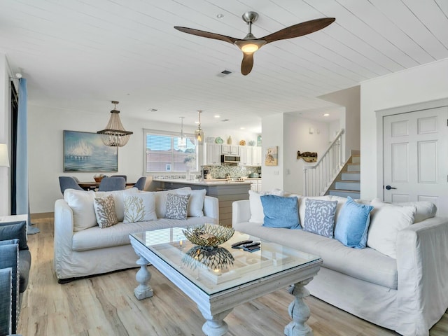 living room with visible vents, stairway, light wood-style floors, a ceiling fan, and wooden ceiling