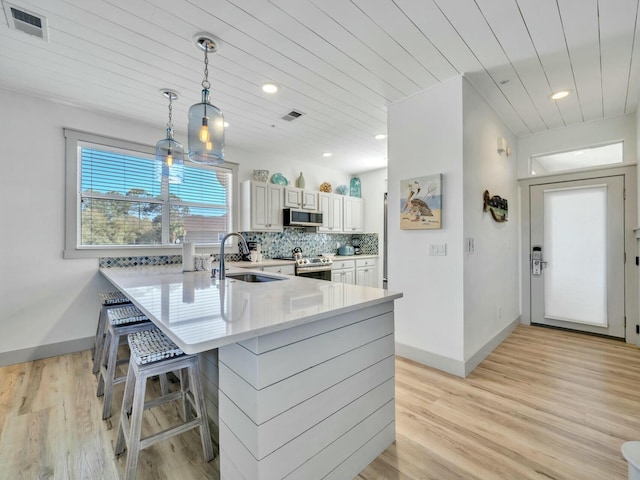 kitchen featuring appliances with stainless steel finishes, a kitchen breakfast bar, a peninsula, a sink, and backsplash