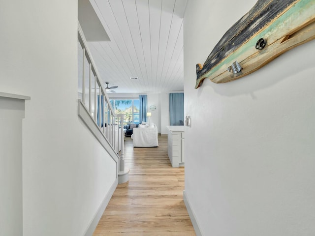 hallway with light wood-style floors, wooden ceiling, stairway, and baseboards