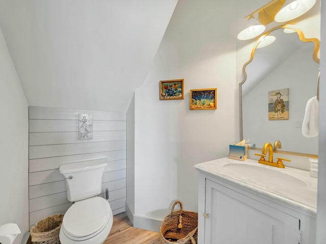 bathroom with lofted ceiling, vanity, toilet, and wood finished floors