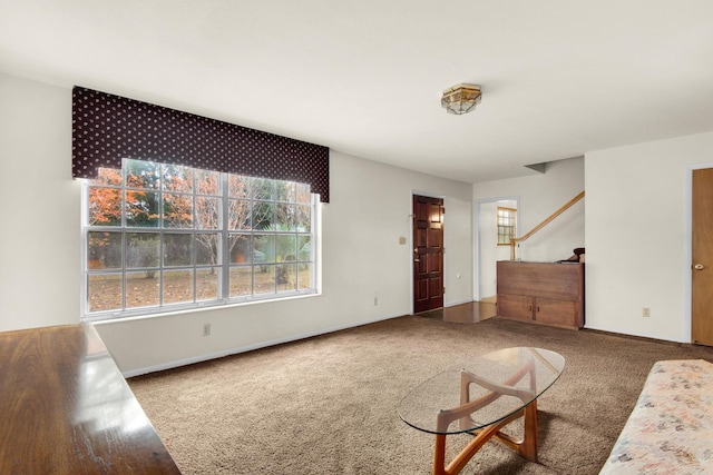 unfurnished living room featuring carpet floors, stairway, and baseboards