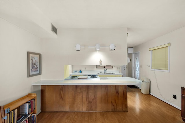 kitchen with a peninsula, wood finished floors, light countertops, and visible vents