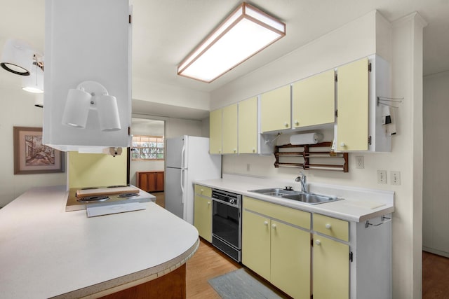 kitchen featuring dishwasher, light wood-style flooring, freestanding refrigerator, light countertops, and a sink