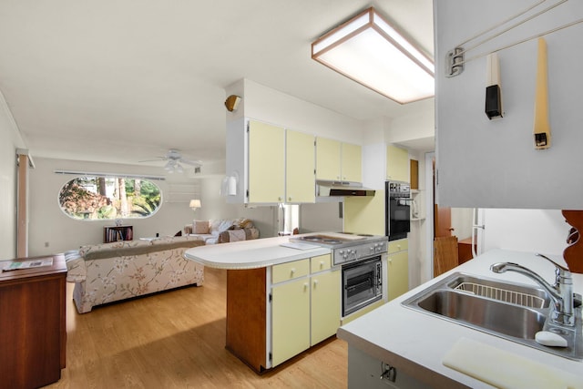 kitchen featuring black oven, a sink, light countertops, and under cabinet range hood