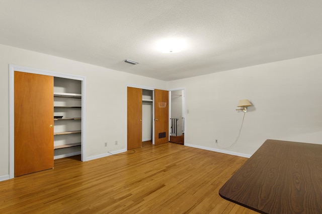 unfurnished bedroom featuring light wood finished floors, two closets, and baseboards