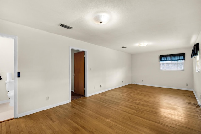 empty room with hardwood / wood-style floors, visible vents, and baseboards