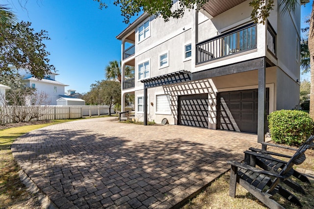 rear view of house featuring an attached garage, a balcony, fence, decorative driveway, and stucco siding