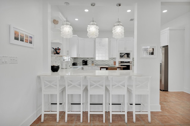 kitchen featuring stainless steel appliances, a peninsula, a sink, a kitchen breakfast bar, and backsplash