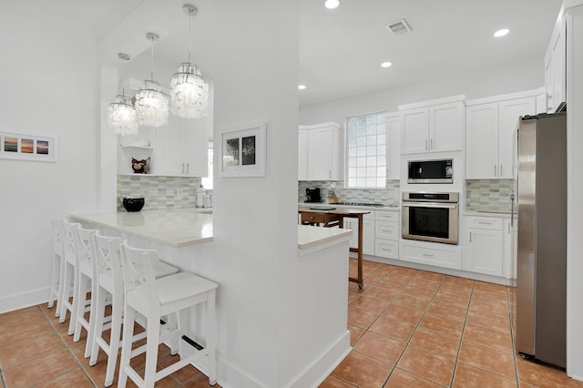 kitchen featuring backsplash, appliances with stainless steel finishes, white cabinets, a peninsula, and a kitchen bar