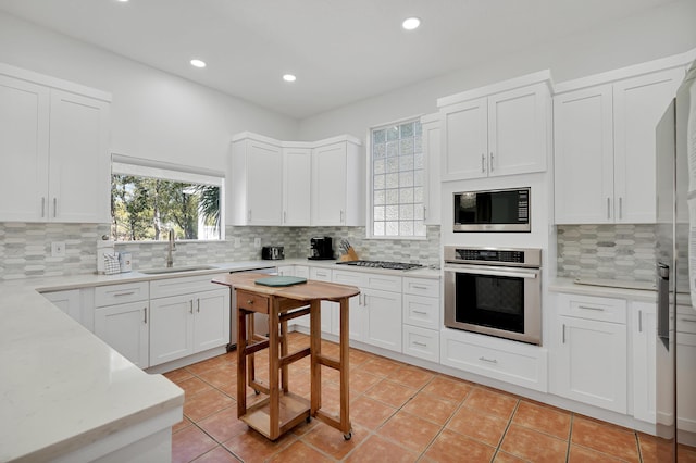 kitchen featuring stainless steel appliances, decorative backsplash, white cabinets, light tile patterned flooring, and a sink