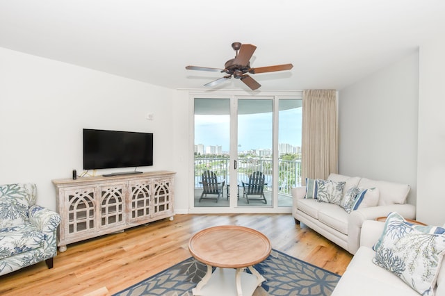 living area with expansive windows, wood finished floors, and a ceiling fan