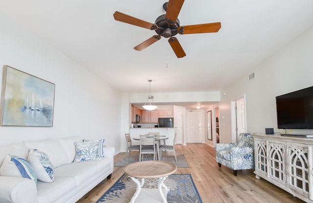 living area featuring baseboards, a ceiling fan, visible vents, and light wood-style floors