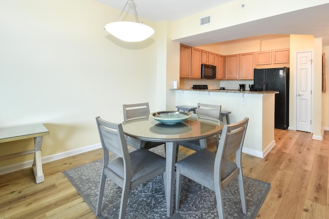 dining room featuring light wood-style flooring, visible vents, and baseboards