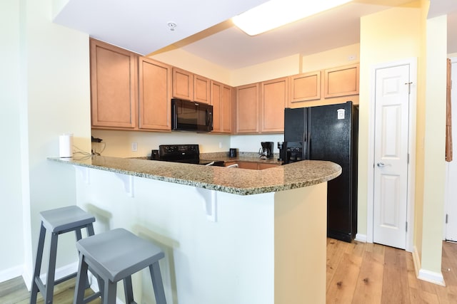 kitchen featuring baseboards, light wood-style flooring, a kitchen breakfast bar, a peninsula, and black appliances