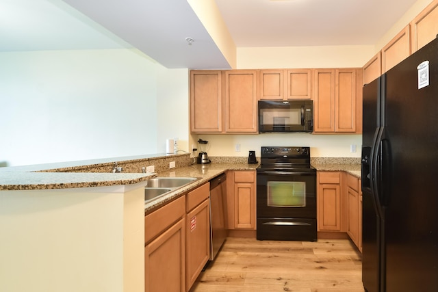 kitchen featuring light wood finished floors, a peninsula, light stone countertops, black appliances, and light brown cabinets