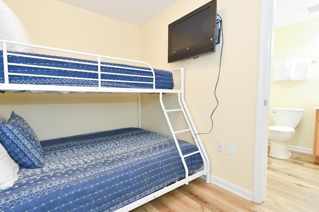 bedroom featuring visible vents, ensuite bath, baseboards, and wood finished floors