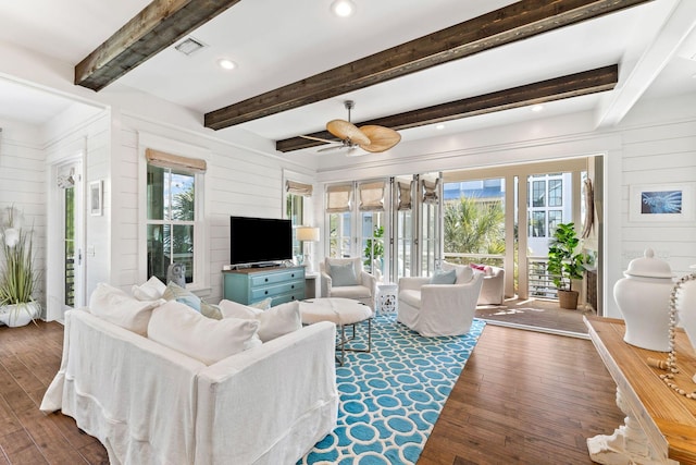 living area featuring ceiling fan, wooden walls, visible vents, beam ceiling, and hardwood / wood-style floors