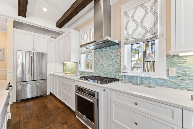 kitchen featuring appliances with stainless steel finishes, beamed ceiling, wall chimney range hood, and white cabinets