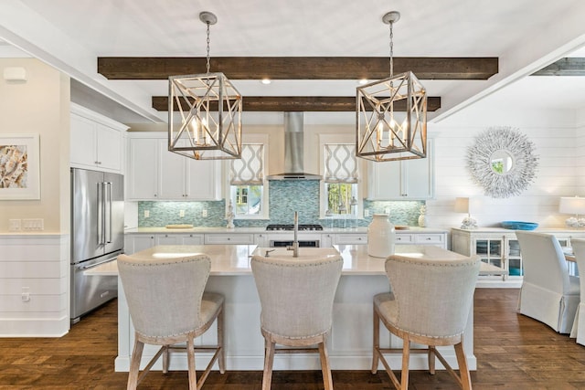 kitchen featuring a chandelier, high end fridge, wall chimney range hood, and dark wood-type flooring