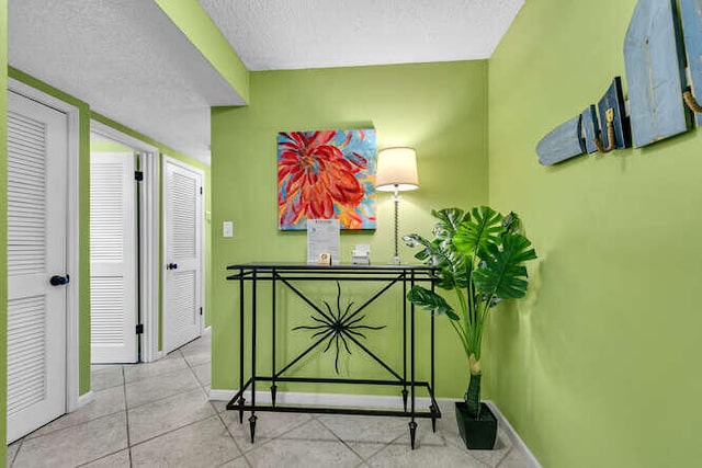 hall with a textured ceiling, tile patterned floors, and baseboards