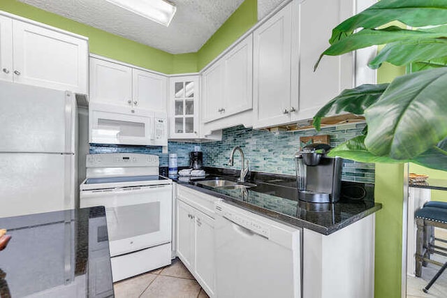 kitchen featuring white appliances, light tile patterned floors, decorative backsplash, white cabinetry, and a sink