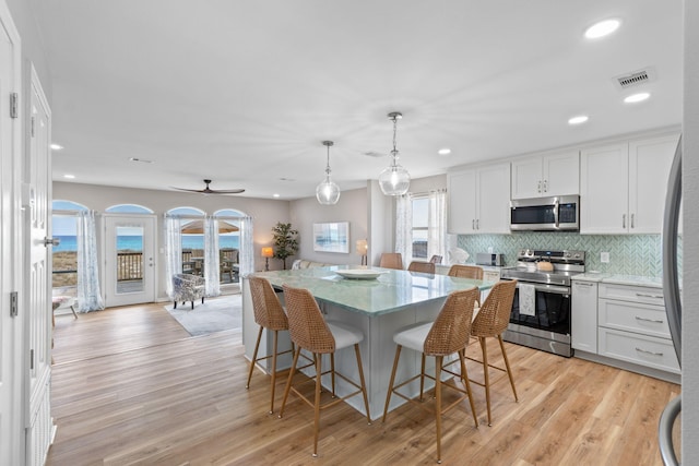 kitchen featuring visible vents, appliances with stainless steel finishes, a breakfast bar, light wood-type flooring, and backsplash