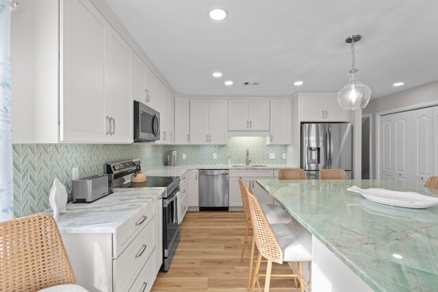 kitchen with stainless steel appliances, light wood-style floors, a kitchen bar, white cabinetry, and a sink