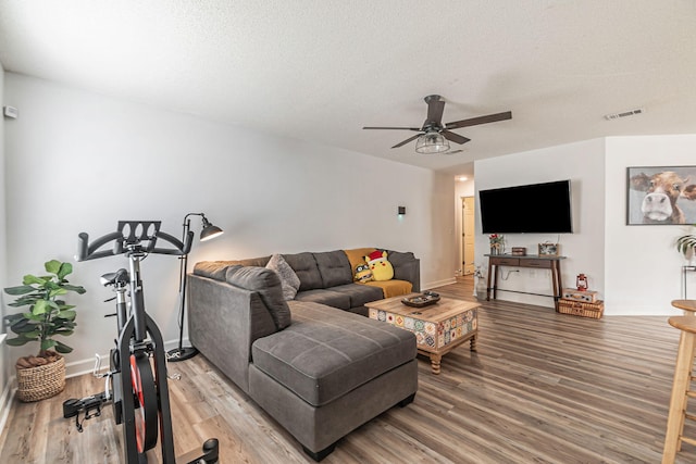 living area with a textured ceiling, ceiling fan, visible vents, baseboards, and light wood-style floors