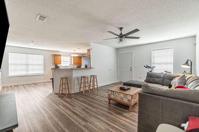 living area with ceiling fan, a textured ceiling, wood finished floors, visible vents, and baseboards